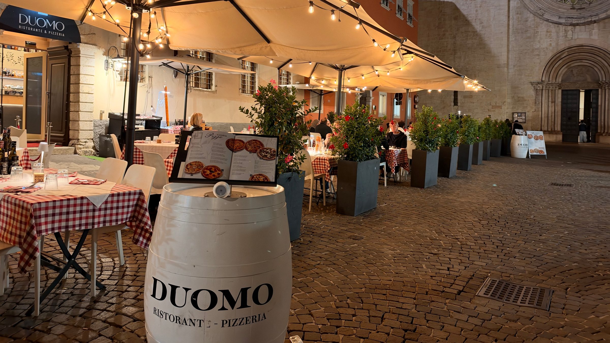 Il dehors del Ristorante Al Duomo di sera, con gli ombrelloni accesi e la botte col marchio